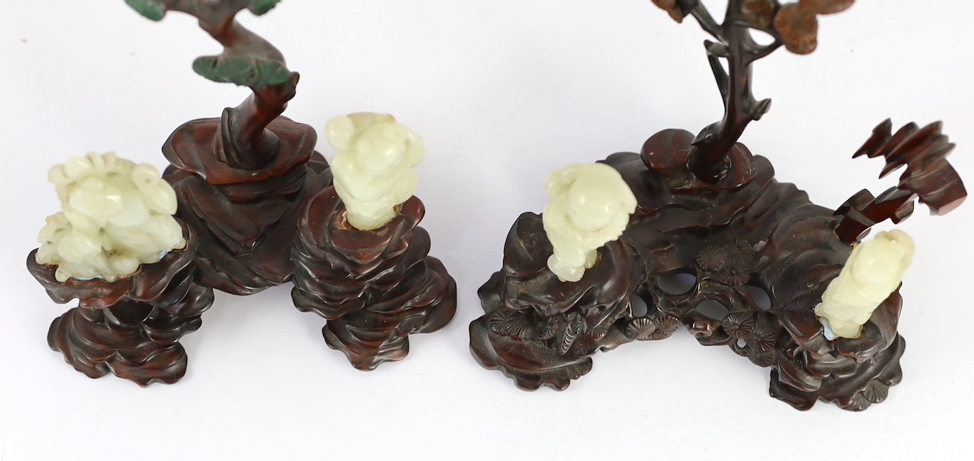 An assembled group of four Chinese pale celadon jade figures, 18th/19th century, displayed on two later wood 'rock-work' stands, total height approximately 19cm high